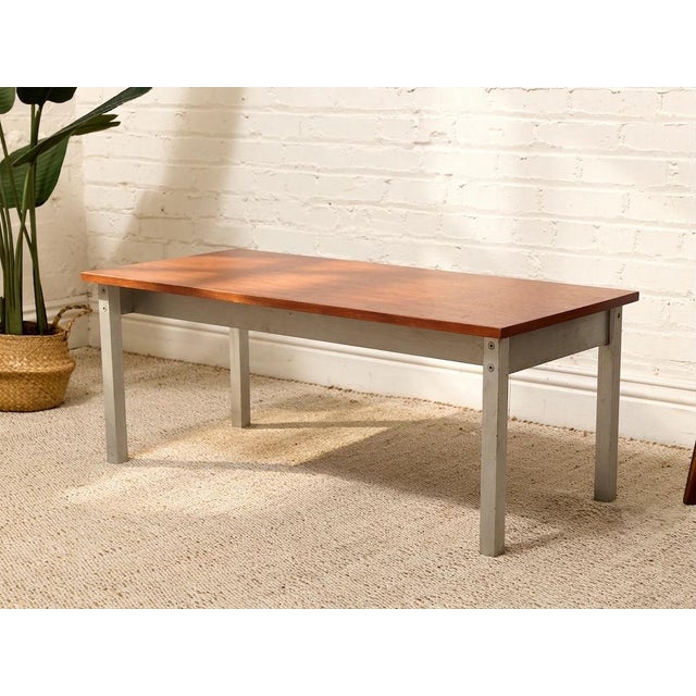 A clean, architectural vintage piece combining a richly grained warm wood top with a simple brushed metal base. The long...