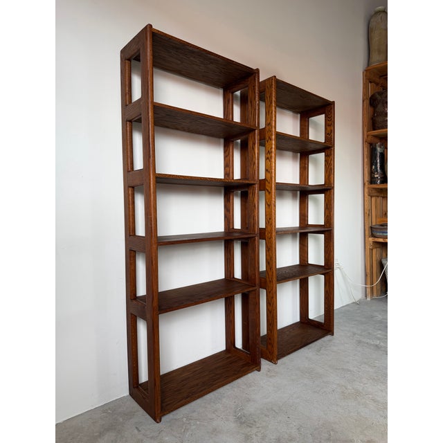 A striking pair of 1970s Mid-Century Modern six-tier bookcases in the style of Lou Hodges, expertly crafted from solid oak...