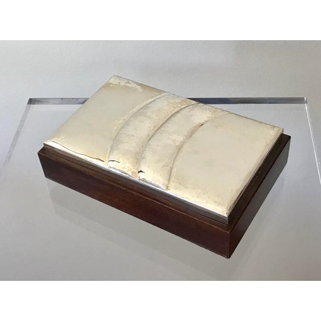 A box with a silver plate lid and satin wood interior. Two shimmering wave-like forms ripple across hand hammered surface...
