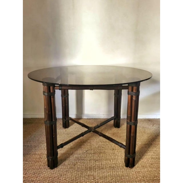 Vintage round smoked glass table with bamboo legs and leather straps.