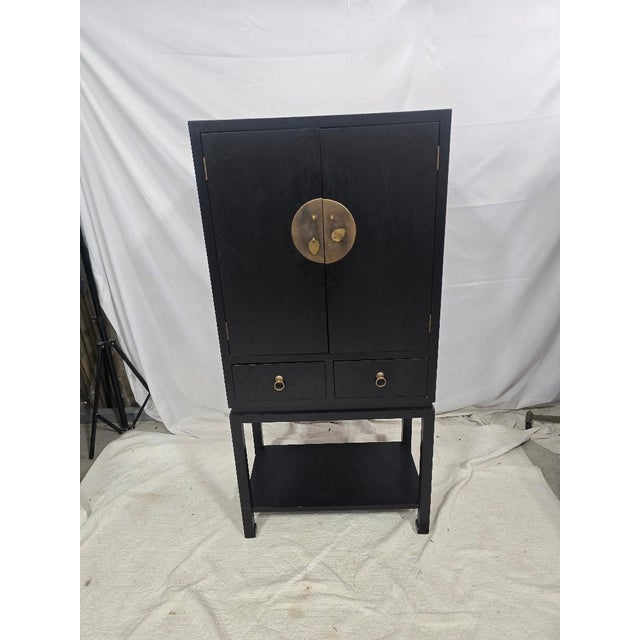 A striking Asian-inspired black lacquer cabinet featuring bold brass medallion hardware, offering a refined blend of...