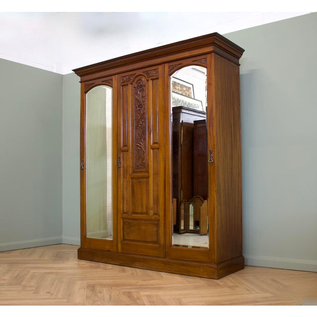 An impressive circa 1900 triple wardrobe in warm-toned walnut, featuring two arched mirrored doors, a richly carved...