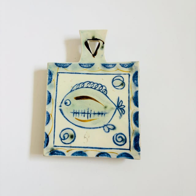 A lovely vintage hand painted ceramic trivet. Feature a fish design in blue and white glazes with a handle on one end....