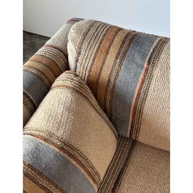 Wrapped entirely in richly textured striped upholstery, this vintage sofa carries a low, architectural silhouette with a...