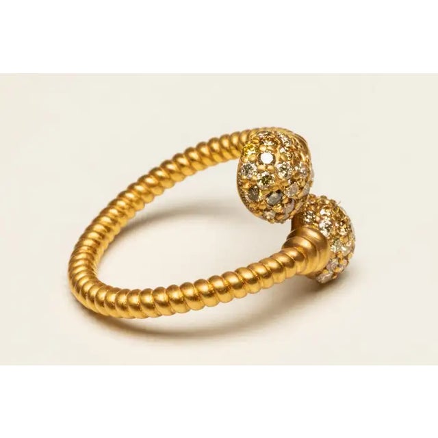 An exceptional ring of two crossed and twisted 18K gold bands ending with balls of round, brilliant cut, pave`-set...