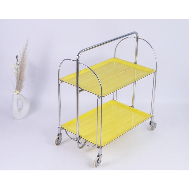Mid-century yellow bar cart made in Germany in the 60's. It has a chrome metal base/mechanism which makes this dinett...