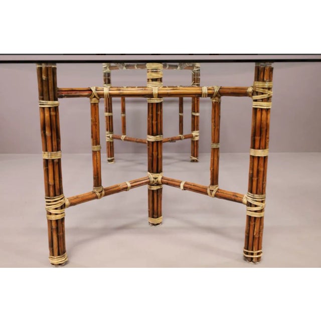 A beautiful, unsigned McGuire Dining Table. Rattan and Leather banded base with a large/heavy glass top. Some banding is...