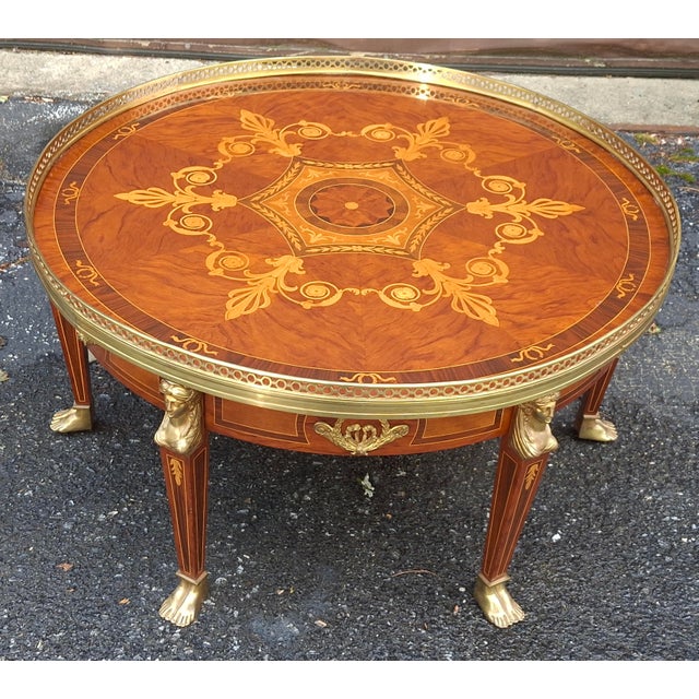 An elegant French Empire round coffee table has beautiful inlaid marquetry with legs of classical caryatids with brass...