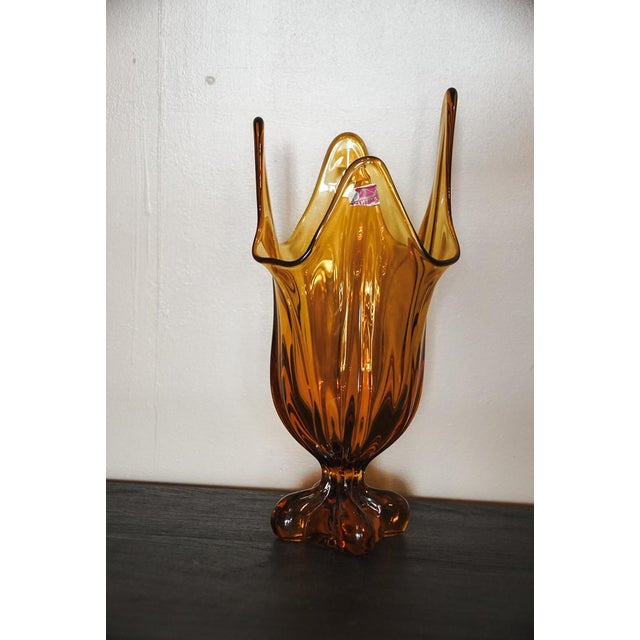 The Viking Glass Epic Amber Drape Swung Glass Vase from the 1960s is a vintage piece of decorative glassware originating...