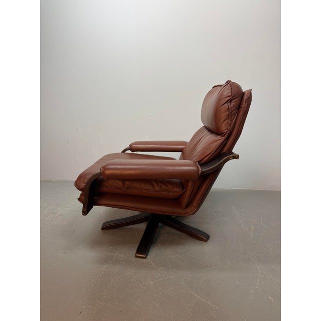 Comfortable swivel lounge chair by Leolux, featuring cognac brown leather upholstery and a sculptural bentwood frame. A...