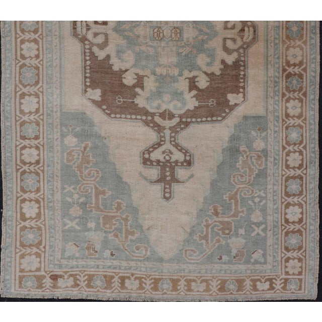 This Turkish Oushak rug has been hand-knotted in wool and features a sub-geometric etched medallion design rendered in...