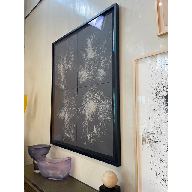 Abstract contemporary artwork with white splatter detailing over a dark ground, framed in a clean black frame. Subtle...