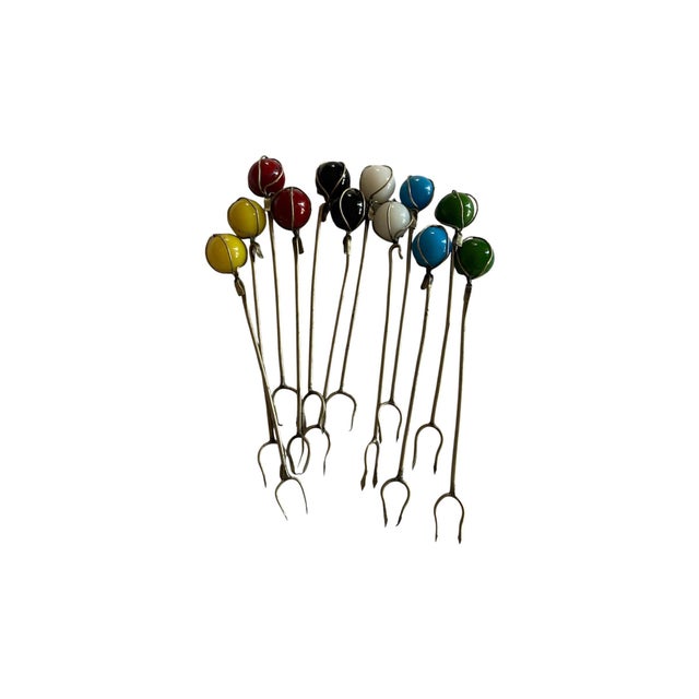 A set of a dozen 4” tall vintage mid 20th century cocktail skewers or forks. Each metal fork is topped with a colorful...