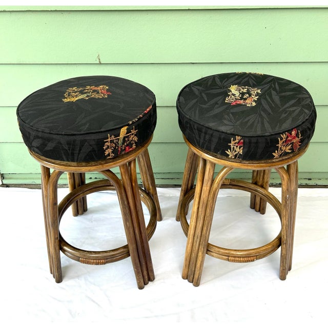 Pair of vintage rattan counter stools featuring dark green upholstered seats with embroidered birds, foliage, and Asian-...