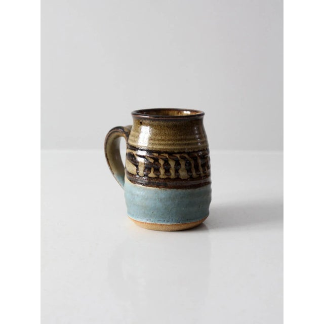 Vintage studio pottery mug featuring a generously sized hand-crafted form with a rich brown and blue glaze and a striking...