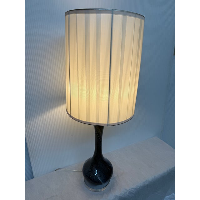 Design Plus Gallery presents a Deep Blue Table Lamp. the lamp has a long ceramic body and matching tall, cylindrical lamp...