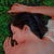 This artwork depicts a serene figure reclining on a lush bed of green grass, her hair cascading around her in gentle...