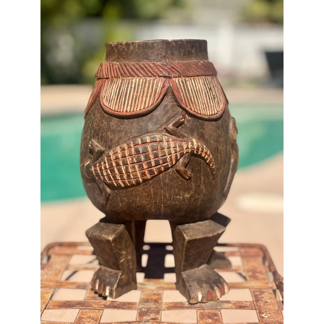 A deeply compelling piece of African material culture, this hand-carved wooden vessel stands on four legs ending in human...