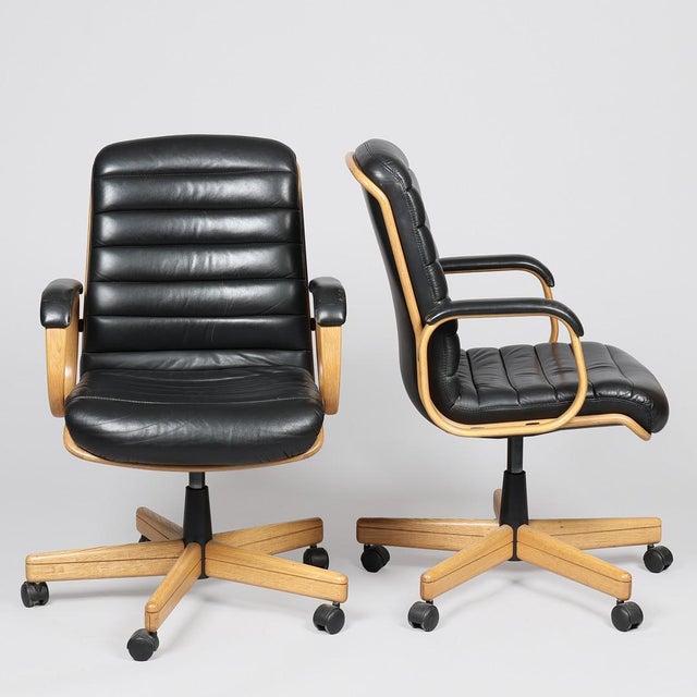 A pair of swivel chairs with oak frame upholstered with black leather and foot with wheels. Designed by Albert Stoll. Made...