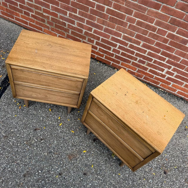 This pair of mid-century modern walnut nightstands features clean lines, sculpted integrated drawer pulls, and tapered...