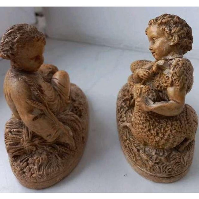 Decorative pair of figurines depicting pastoral/devotional shepherd children in reclining poses, richly modelled with...