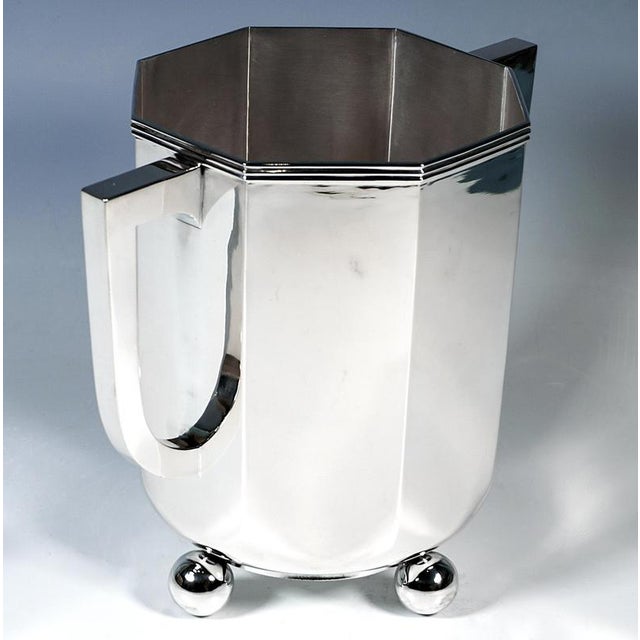 Elegant silver vessel with a round base standing on four ball feet, transitioning into an octagonal body with smooth...