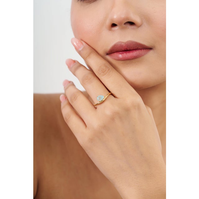 This solitaire ring features a stunning 1-carat pear-cut light teal paraiba tourmaline, beautifully set in a 18k yellow...