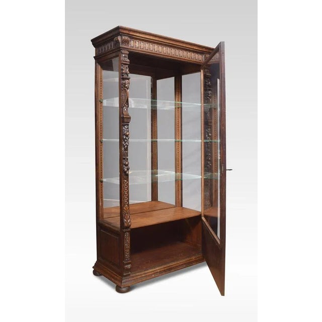 Oak display cabinet the projecting molded cornice above a large glazed door encased in carved frame with winged cherubs...