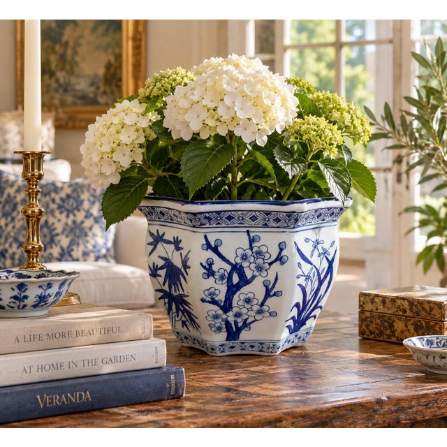 A classic blue and white porcelain planter, rendered in a softly faceted, scalloped form that feels both tailored and...