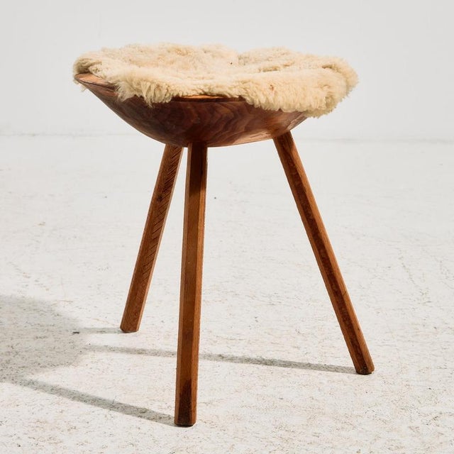 Handcrafted milking stool with three legs and a sheepskin-covered seat. The surface shows scratches and wear in places.