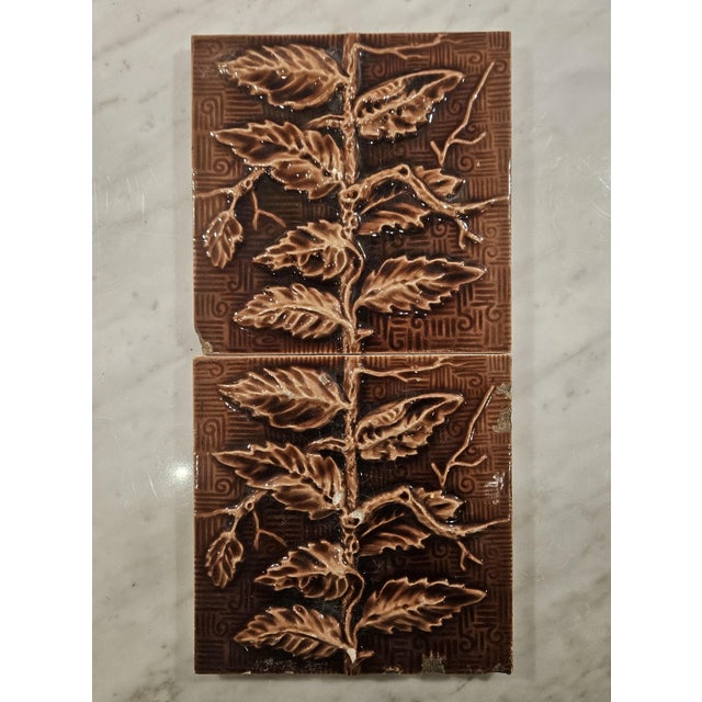 A pair of Hamilton Tile company "Vine and Leaf" tiles in brown and light tan. They have a swirl pattern behind them and...