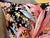 Large pink and turquoise tropical leaves rise from a deep black ground, surrounded by orange, gold, and mauve botanical...