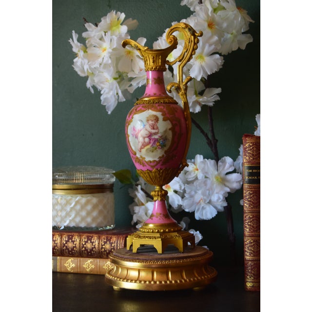 An elegant antique Sèvres-style porcelain ewer featuring a vivid pink ground with elaborate gilt decoration and an oval...