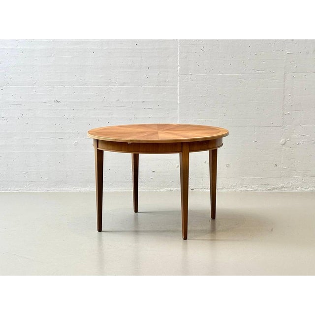 An elegant, round cherry wood dining table that impresses with its fine veneer work and balanced proportions. The tabletop...