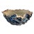 A bowl as sculpture, its ruffled edge folding like waves caught mid-motion. A deep blue glaze, dark and lustrous, clings...
