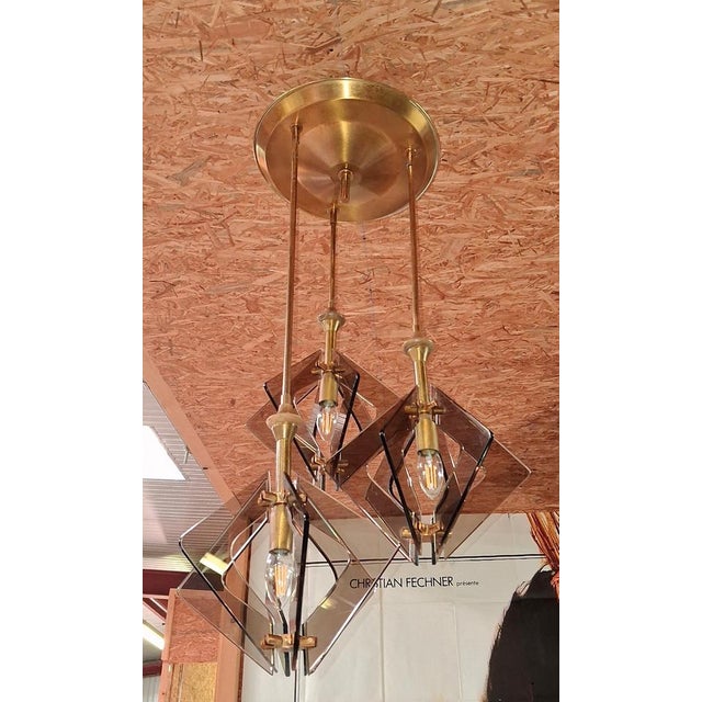 An elegant, modernist pendant light from the 1970s featuring three light sources arranged at different heights. The gold-...