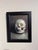 Busted Jaw presents a striking depiction of a skull, rendered in oil on linen board. The soft, diffused lighting enhances...