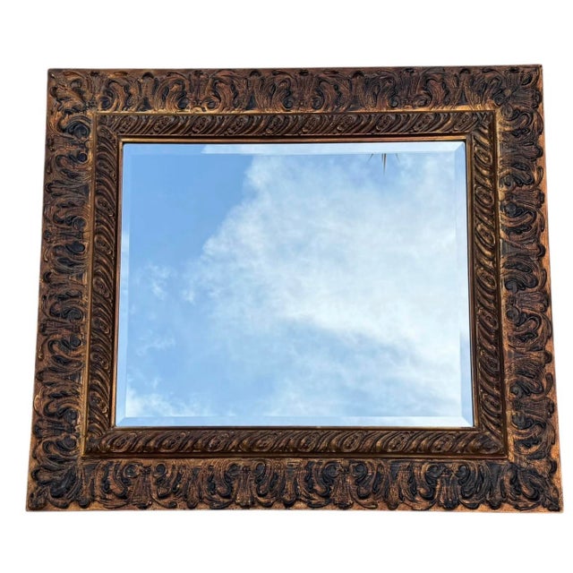 Vintage beveled wall mirror by Carolina Mirror Company featuring an ornate deeply carved frame with a warm gilt finish and...