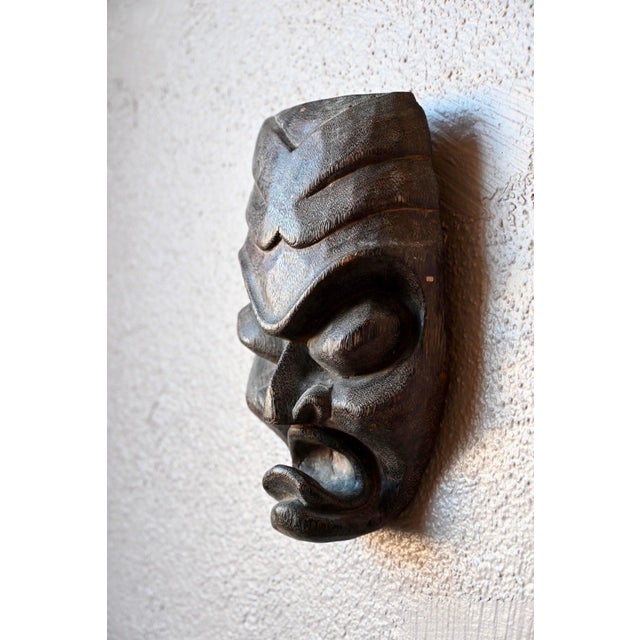 This African mask, carved from a single piece of dense, dark wood, is crafted with remarkable precision and sensitivity....