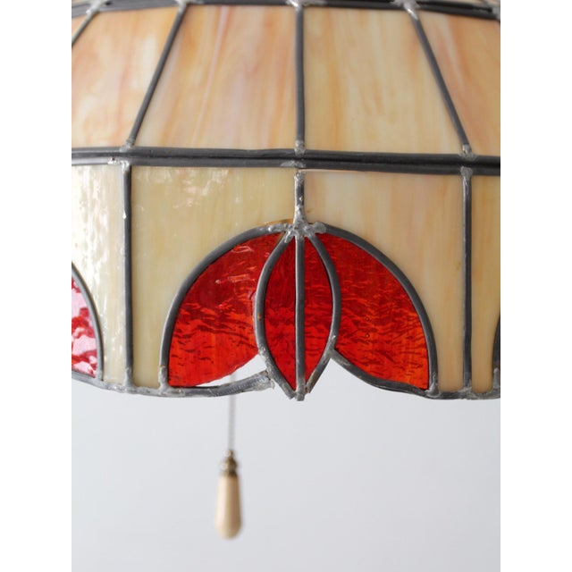 A vintage stained glass hanging pendant light featuring warm cream marbled glass and rich red accent panels in a classic...