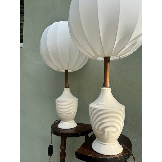 A matched pair of white ribbed ceramic urn-form table lamps, each on a hand-turned barley twist wooden stand, fitted with...