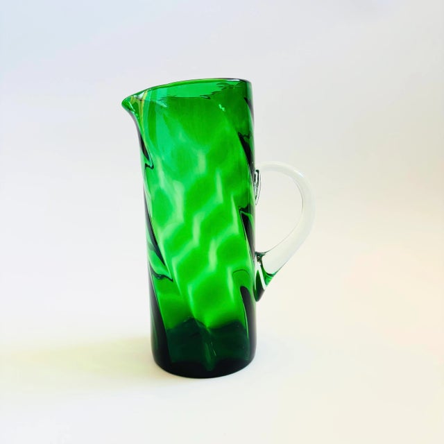A vintage blown glass pitcher. Lovely emerald green color to the glass with a swirl design. Clear handle.