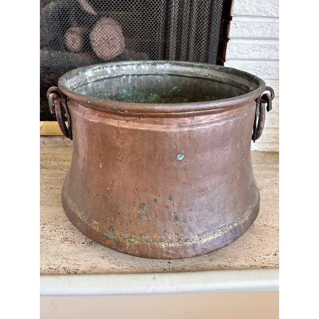 A substantial 19th-century hand-hammered copper cauldron featuring hand-forged iron swing handles and beautiful timeworn...