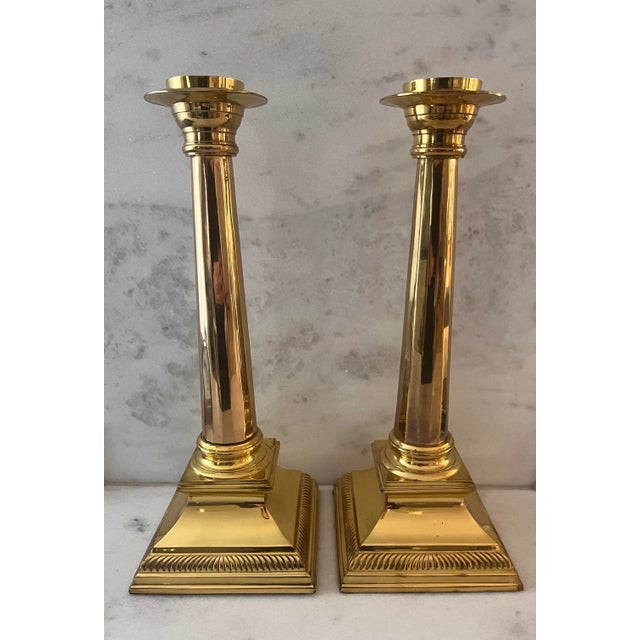 Set of 2 tall and heavy vintage brass column neoclassical candlestick holders with square bases and ridged detailing.