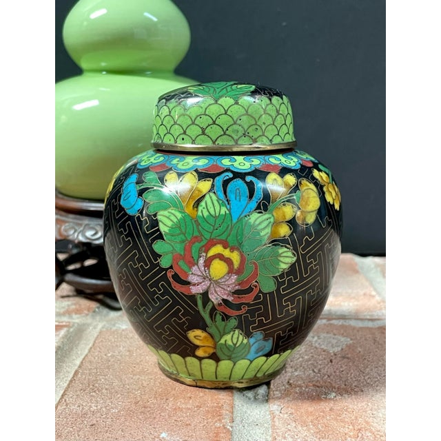 Small vintage handmade cloisonné lidded jar from China features brightly colored floral design against black background....