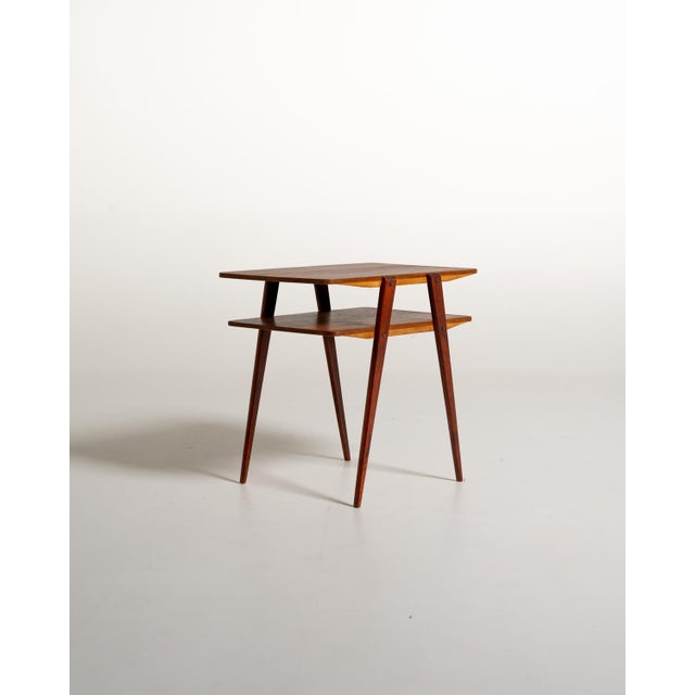 Lightweight, two-tier structure with teak tops and slender, slanted mahogany legs, punctuated by exposed screw joints....