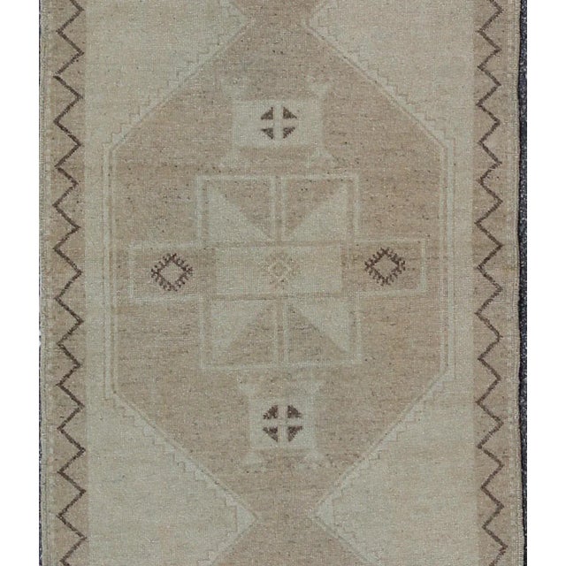 This Oushak runner presents three unique medallions laid out across a solid beige field. Each medallion contains a...