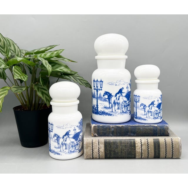 Charming set of three vintage white milk glass apothecary jars made in Belgium, each decorated with rich cobalt blue...