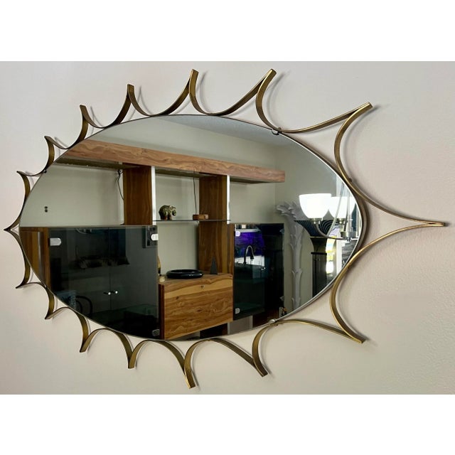 Iconic mid-century modern wall mirror. This piece is a large oval wall mirror, with a thick brass sunburst style surround....