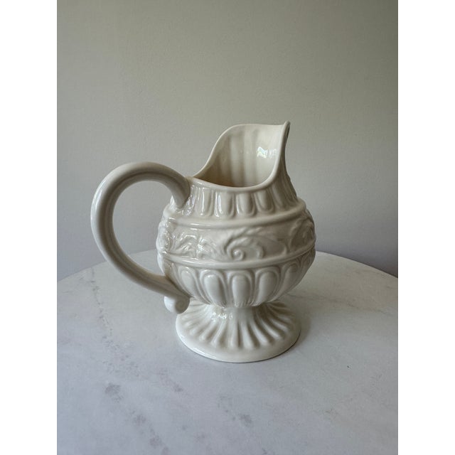 A charming vintage creamware pitcher standing 8" tall. This footed jug features layered embossed relief decoration...